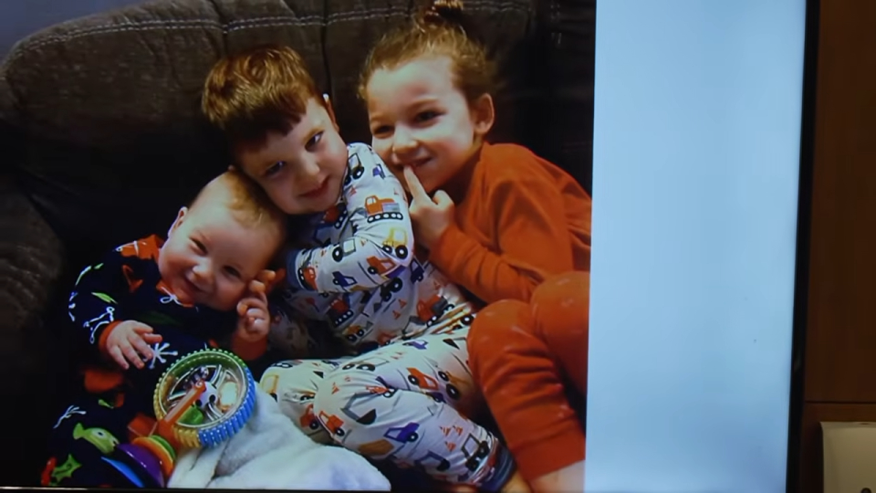 Three children, two older and one infant, in pajamas, sitting together on a couch.