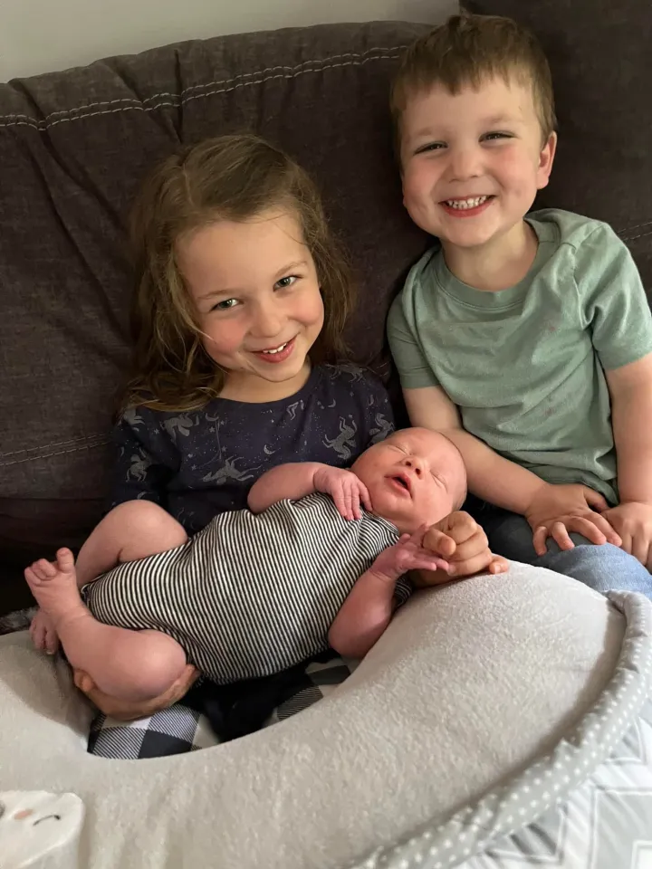 Three children, a girl, a boy, and a baby, posing for a picture on a couch.