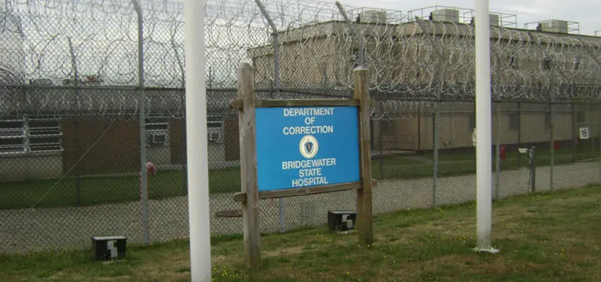 Bridgewater State Hospital sign in front of a chain-link fence topped with barbed wire.