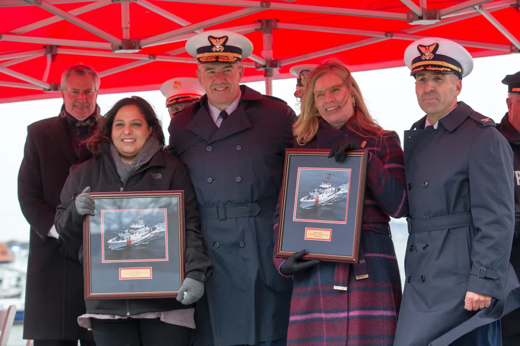 Lisa Palazzo and Angela Danz hold framed images of the future Coast Guard Cutters named after their deceased spouses.
