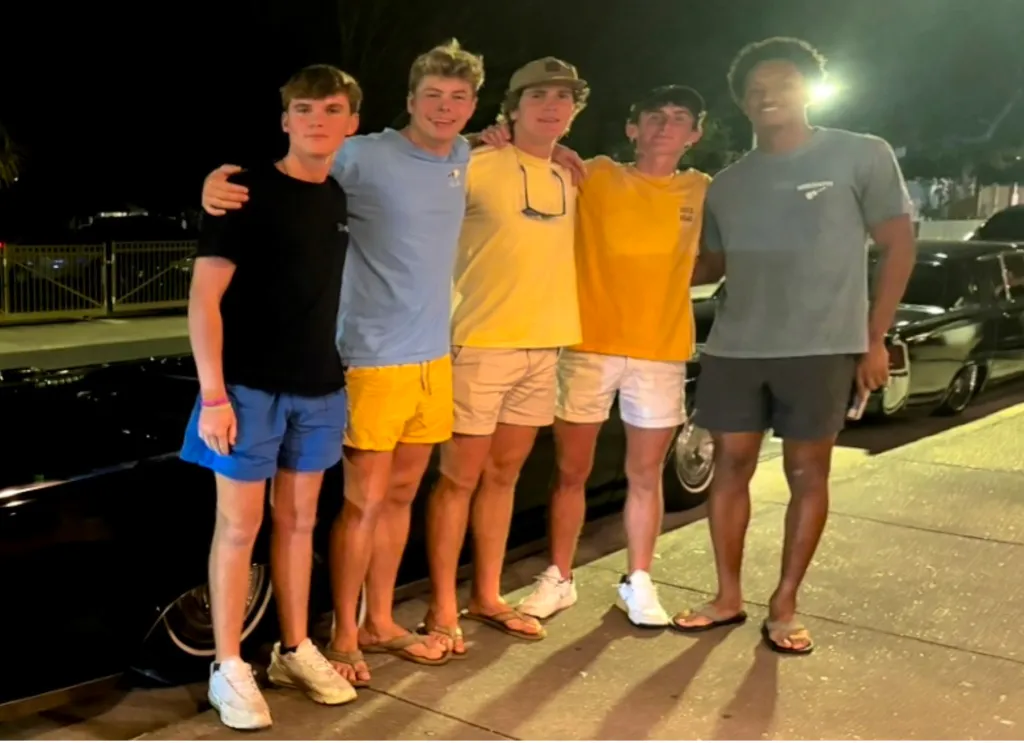 Five young men, including Nolan, Warren, Jax, and Morgan, standing next to a car at night.