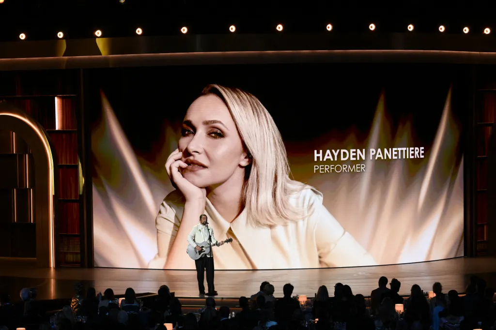 Noah Kahan performing with a large image of Hayden Panettiere projected behind him.