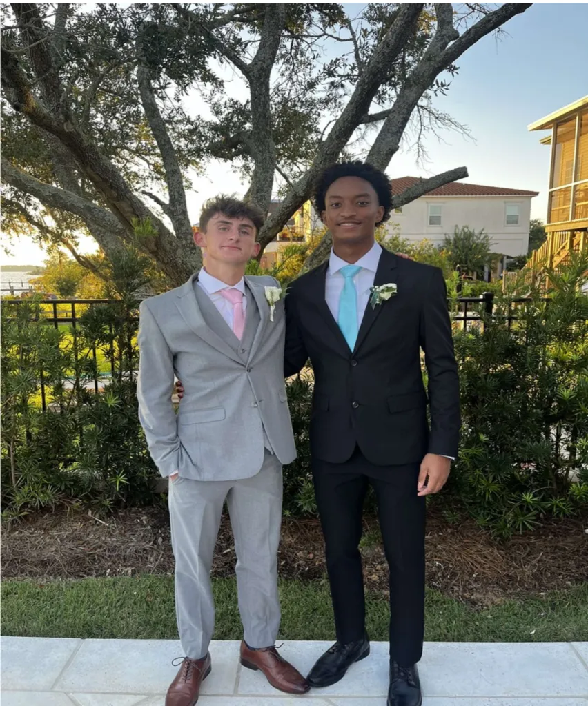 Two young men standing outside, wearing suits with boutonnieres.