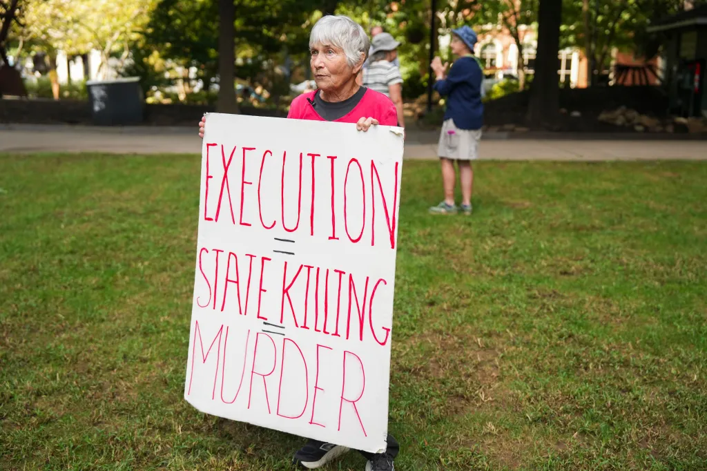 Carol Nickel holds a sign reading "EXECUTION = STATE KILLING = MURDER" during a vigil for Christa Pike in Krutch Park.