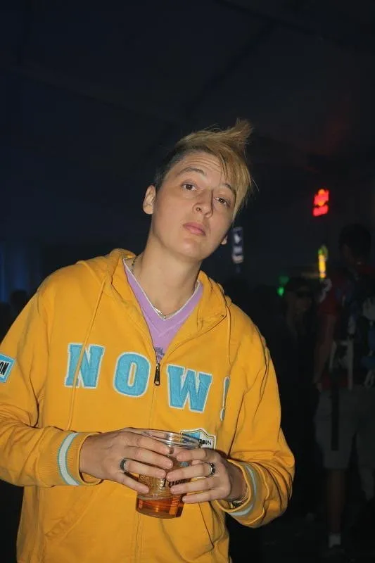 Taylor Winters wearing a yellow hoodie and holding a drink, before transitioning.