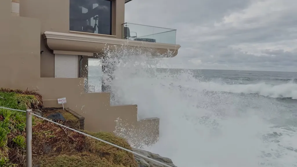High tides crash against a coastal home in Laguna, sending white water splashing up its walls under an overcast sky.
