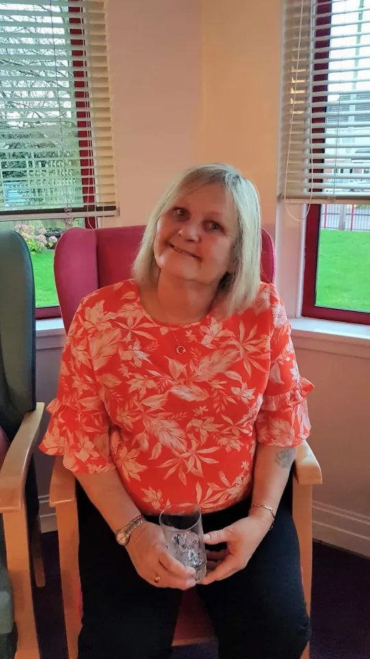 Val McDowell sitting in a chair holding a glass of ice.