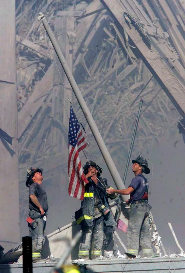NEW YORK - SEPTEMBER 11: (EDITORIAL USE ONLY - NO COMMERCIAL SALES) Brooklyn firefighters George Johnson (left), Daniel McWilliams( center) and Billy Eisengrein raise a U.S. flag at the site of the World Trade Center after two hijacked commercial airliners were flown into the buildings September 11, 2001 in New York. (PH๏τo by 2001 The Record (Bergen Co. NJ)/Getty Images)