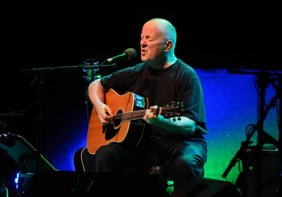 Christy Moore biểu diễn trên sân khấu, chơi đàn guitar acoustic vào micro tại Nhà hát Bord Gais Energy ở Dublin, Ireland.