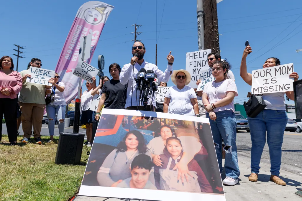 A lawyer speaks at a press conference next to a picture of a missing woman, surrounded by family and community members holding signs that read "Where is Yuli?" and "Our mom is missing."