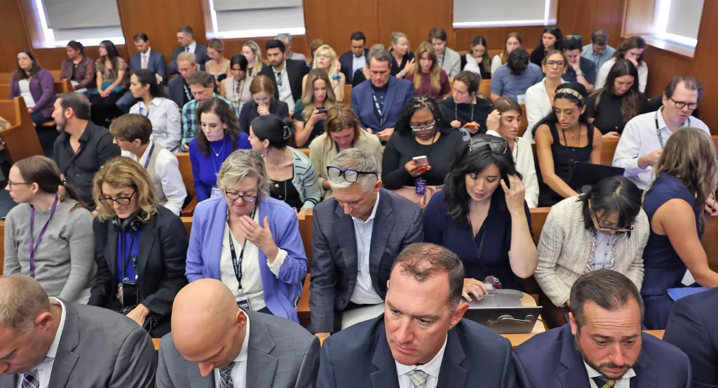 A packed courtroom gallery with spectators seated in wooden pews.