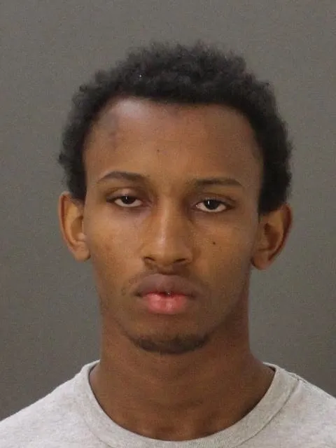 A mugshot of a young Black man with short dark hair and a light gray t-shirt.