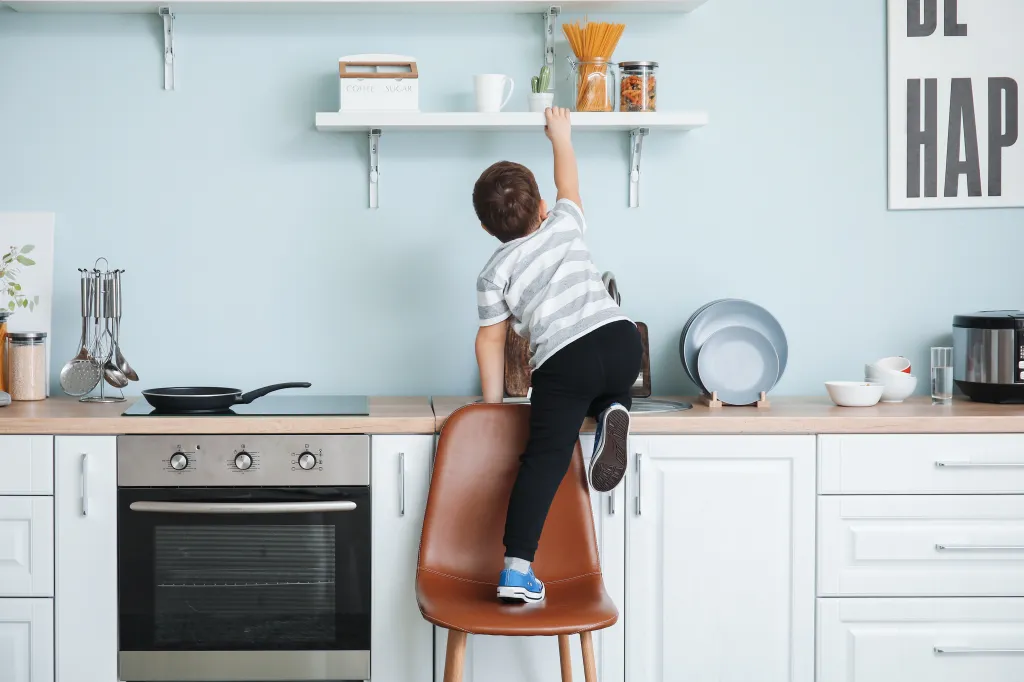 A little boy tries to reach out for pasta at home on a kitchen counter.