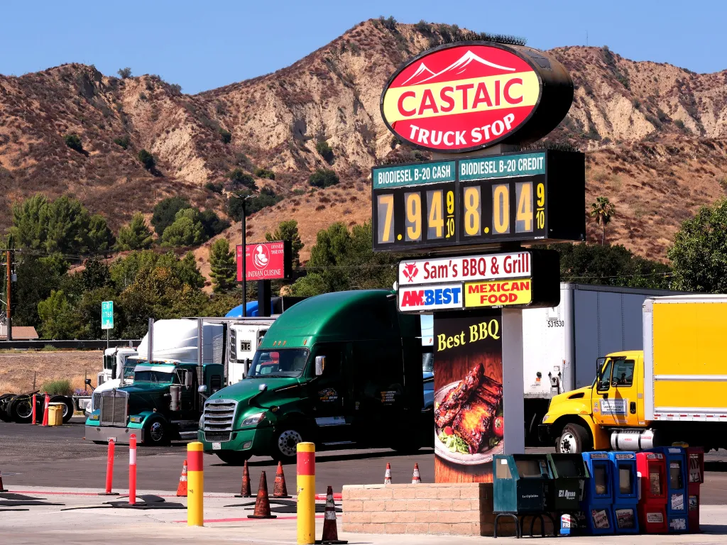 A large sign at the Castaic Truck Stop displays diesel prices of $7.94 cash and $8.04 credit, with semi-trucks parked in the background against dry hills.