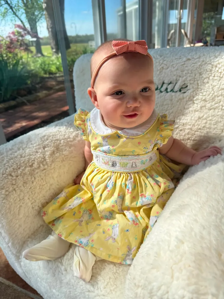 Scottie Crowell sitting in a chair wearing a yellow dress and a pink bow.