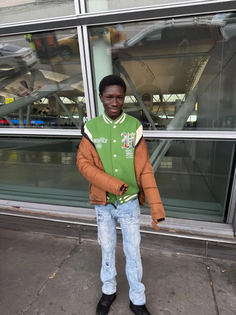 Javits Frimpong stands in front of a glass window wearing a green and cream varsity jacket and a brown jacket.