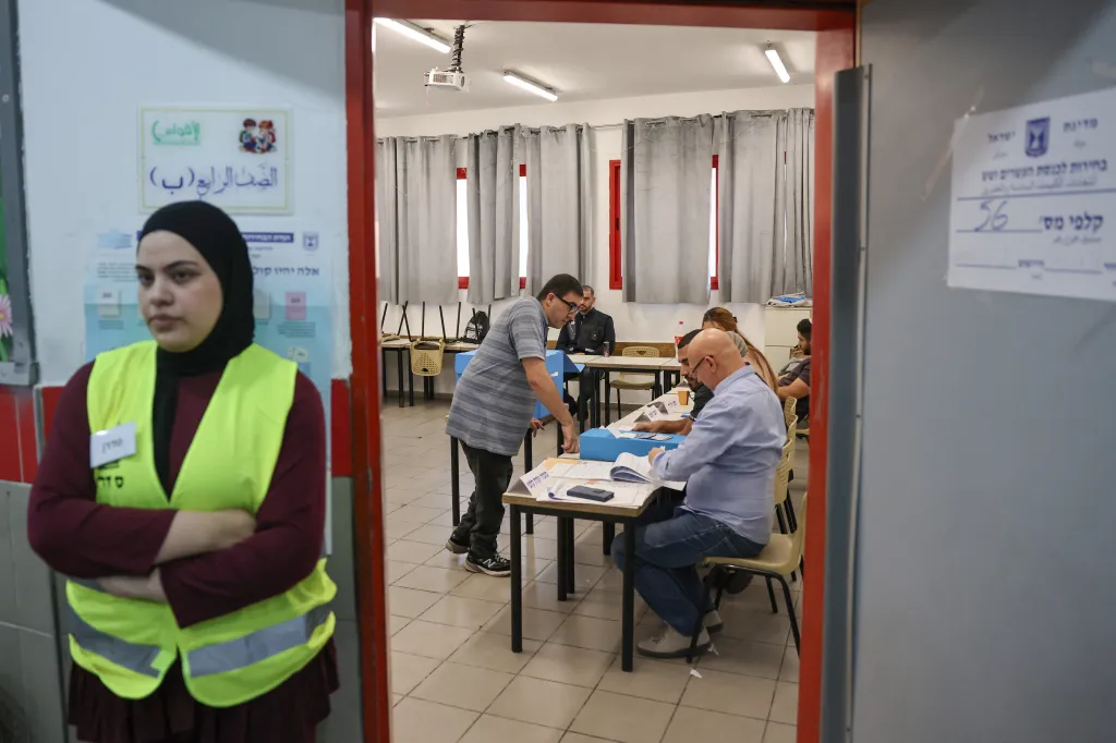 A man registers to vote at a polling station in the Arab-Israeli town of Umm al-Fahm, Israel, with a poll worker in a yellow vest standing in the foreground.