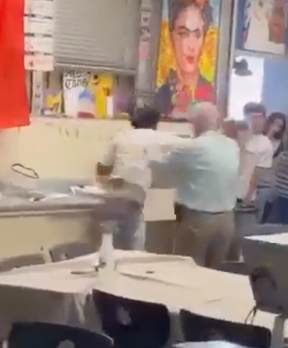 A video still shows a fight inside a high school classroom with a teacher trying to intervene.