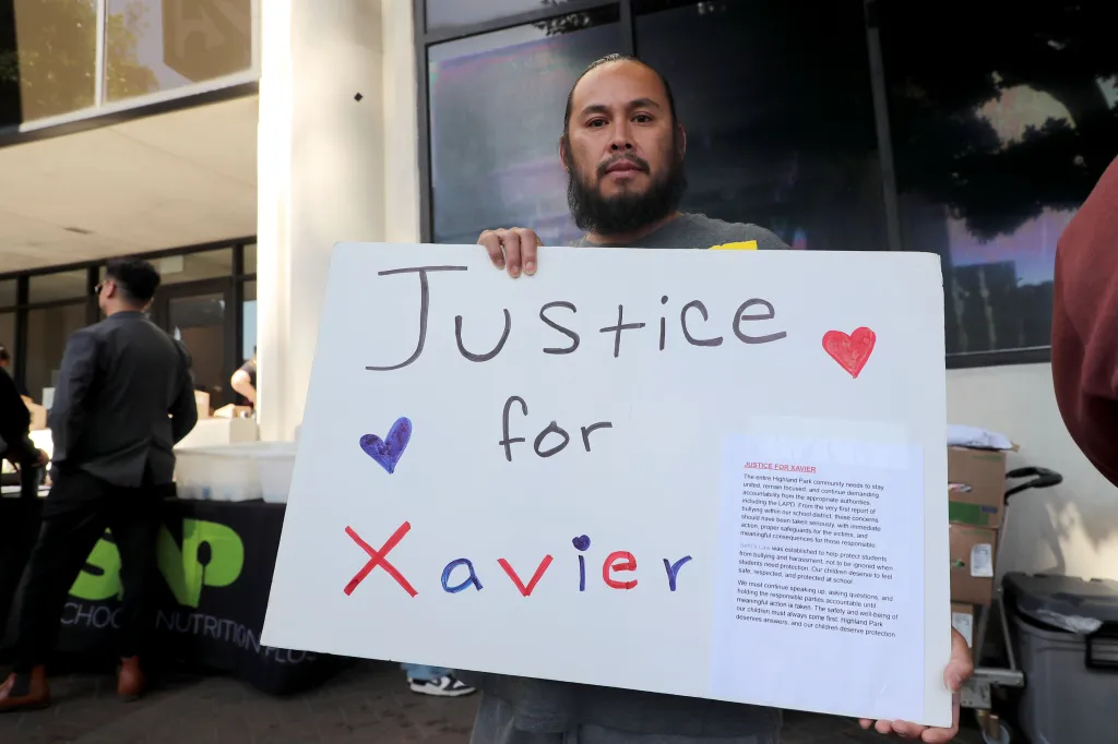William Amaya holding a sign that reads "Justice for Xavier" with a printed flyer attached, during a protest outside the LAUSD building.