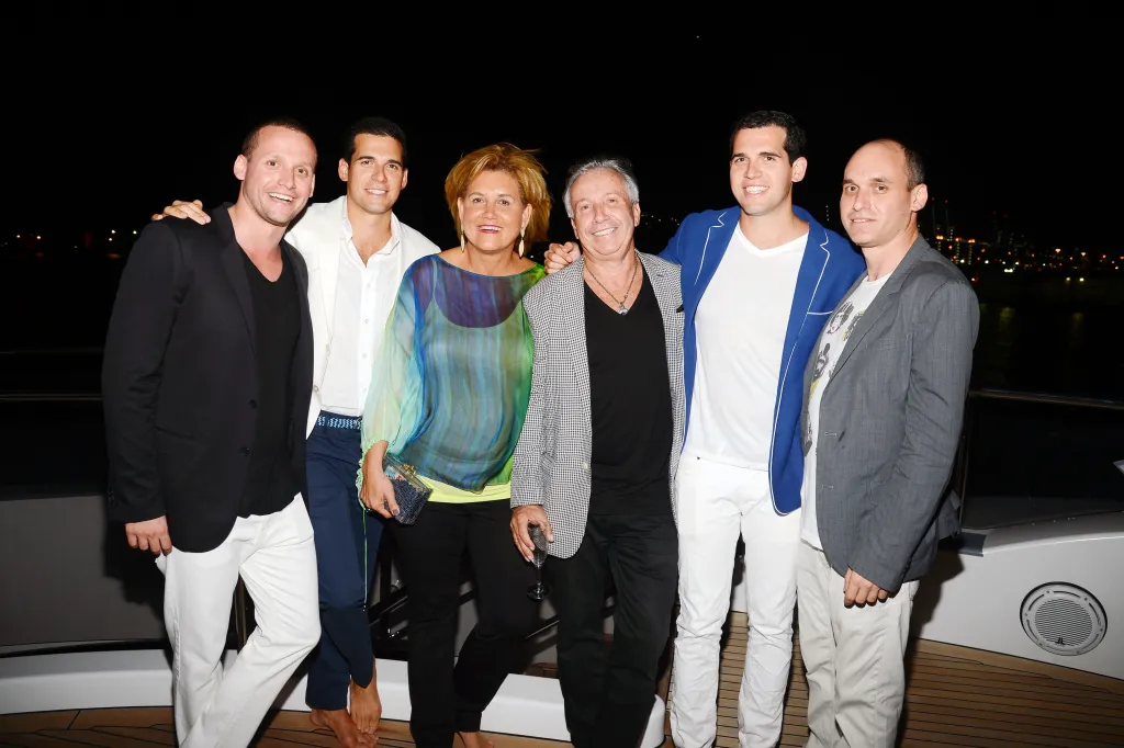 Tal Alexander, Oren Alexander, Orly Alexander, Colin Callender, Patrick Alexander, and Niv Alexander pose together at a reception aboard a motor yacht.