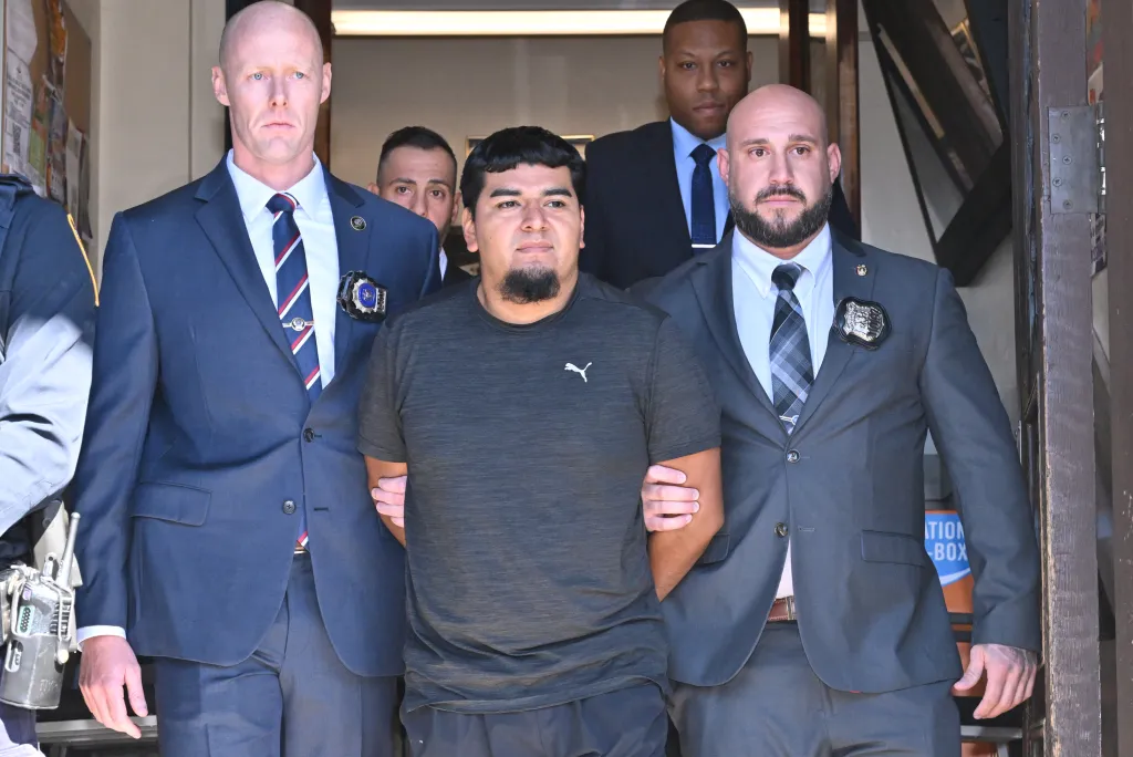 Rogelio Lozano-Garita, in handcuffs and flanked by detectives, being led from the police station house.
