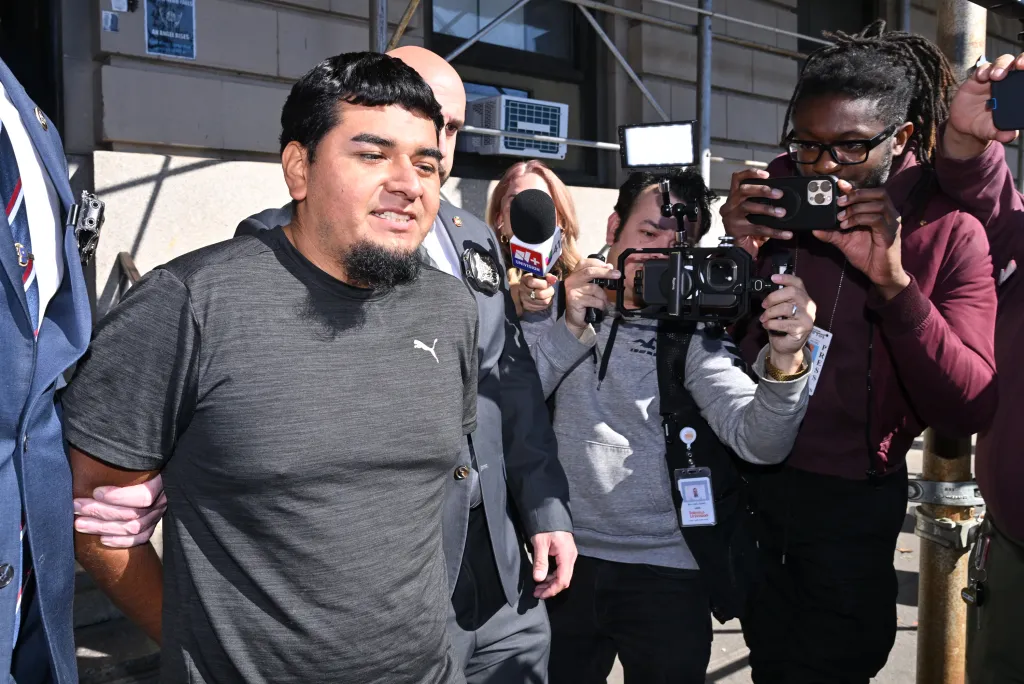 Rogelio Lozano-Garita, in handcuffs, is escorted by police amid a media scrum.
