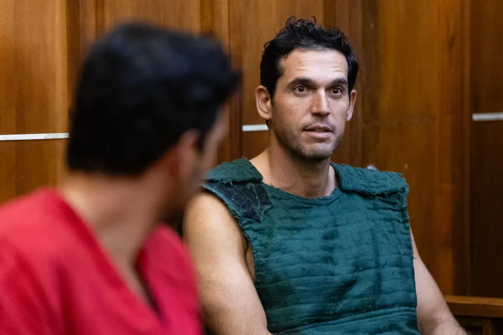 Oren Alexander, wearing a green vest, and his brother Alon Alexander during a bond hearing in a wood-paneled courtroom.