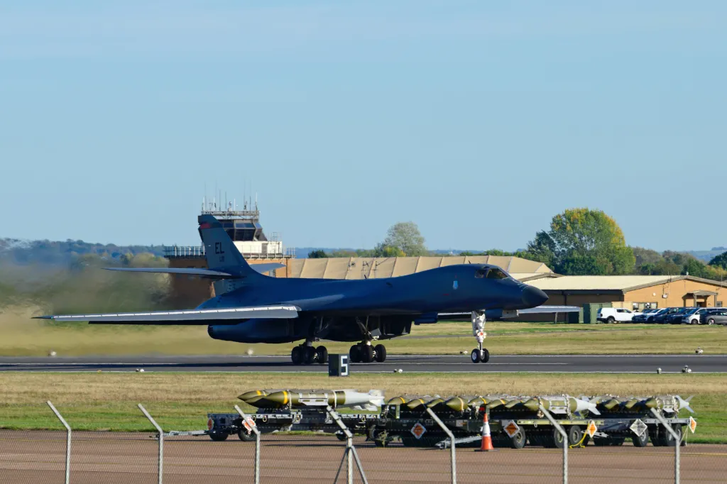 A Rockwell B-1 Lancer heavy bomber prepares to depart from a runway at RAF Fairford, with munitions sitting nearby on carts.