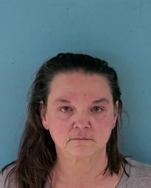 Mugshot of a middle-aged woman with dark hair against a blue background.