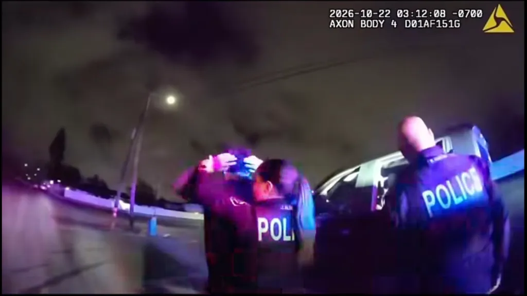 Body-worn camera footage showing police officers detaining a suspect at night near a patrol vehicle.