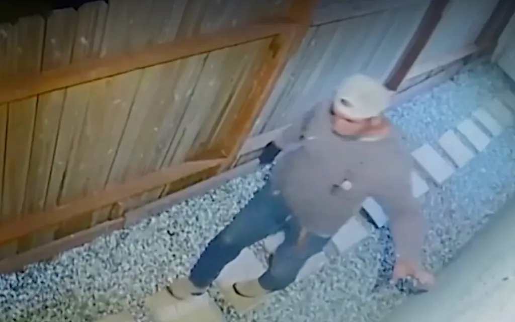 Surveillance footage showing a man walking alongside a wooden fence in a backyard.