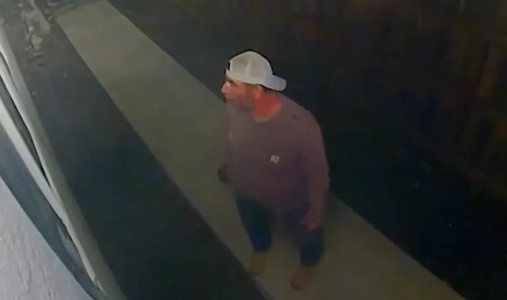 Surveillance footage of a man wearing a baseball cap peering through a window.