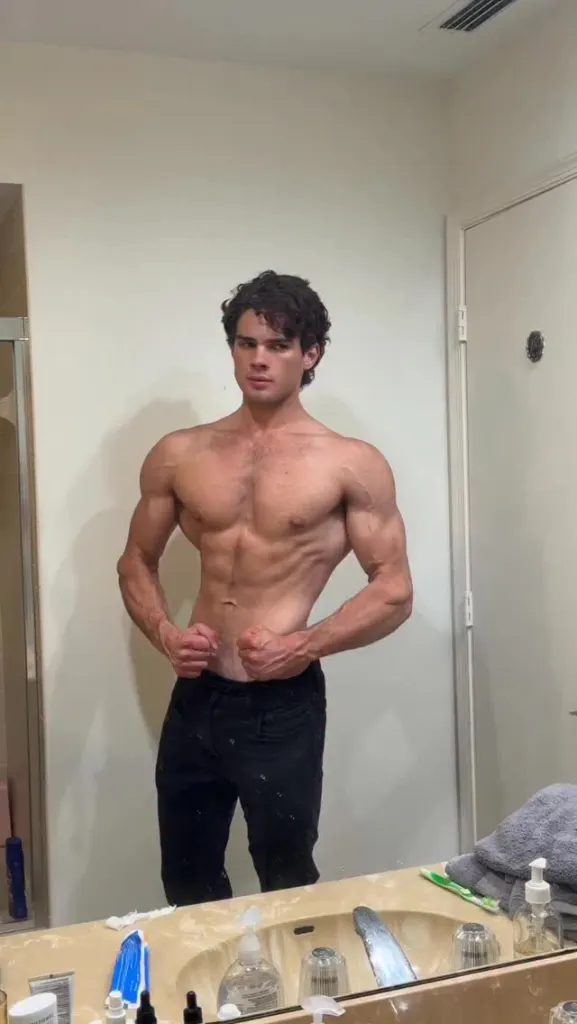 Looksmaxxing influencer Braden Peters, also known as Clavicular, poses in a mirror, showcasing a muscular physique.