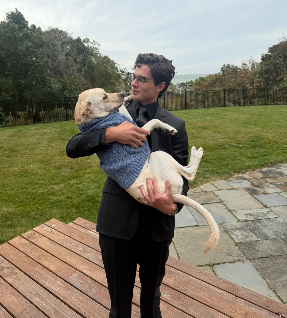 Braden Peters in a black suit holding his dog, who is wearing a blue sweater.