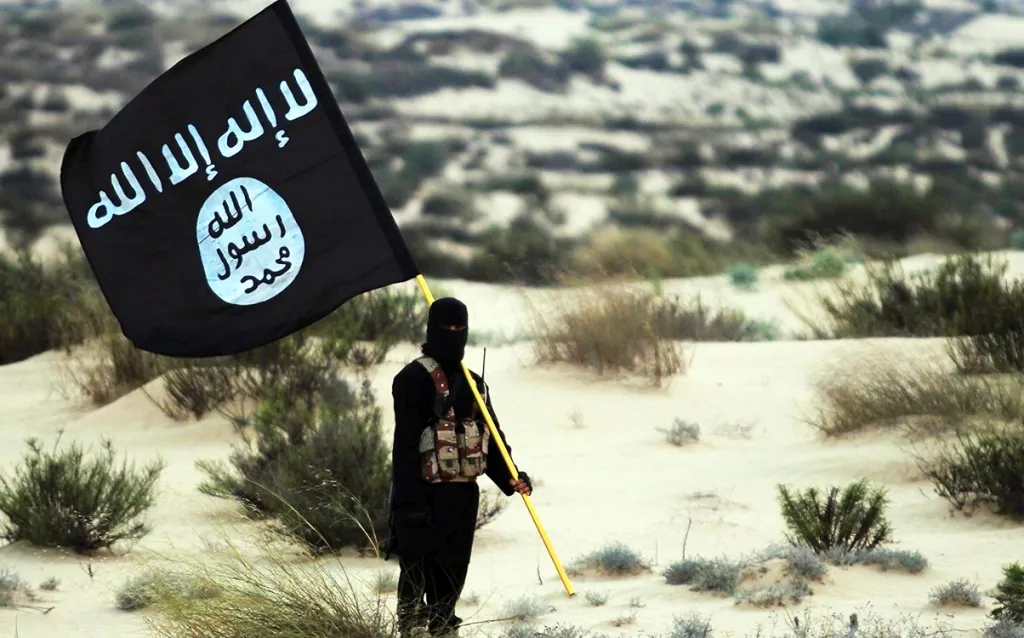 A masked Islamic State soldier holds the ISIL banner in the desert.