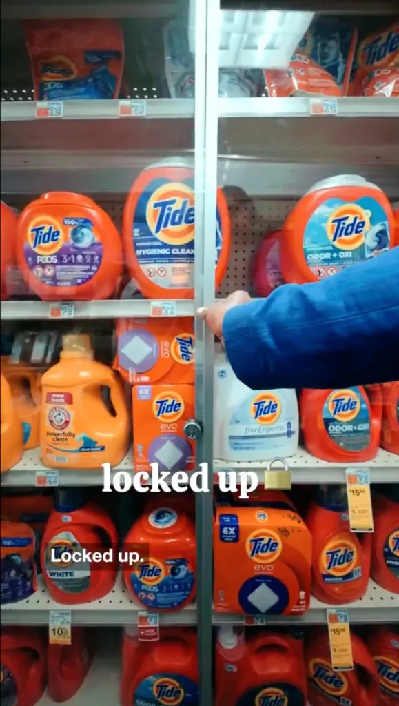 A person in a blue jacket reaches for a locked glass display case holding laundry detergent.