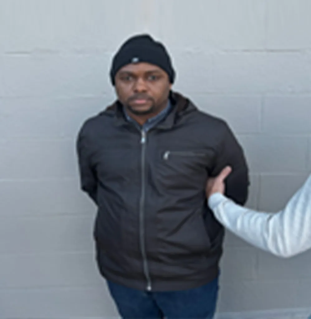 Wilbert Jean-Baptiste stands against a wall in handcuffs after his arrest by U.S. Immigration and Customs Enforcement.