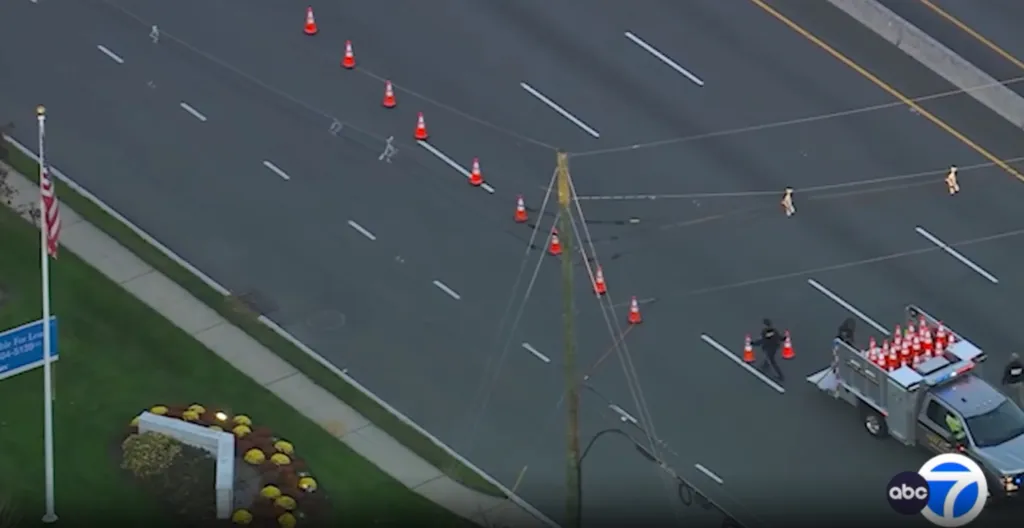 Aerial view of a highway with a line of traffic cones being set up by a utility truck.