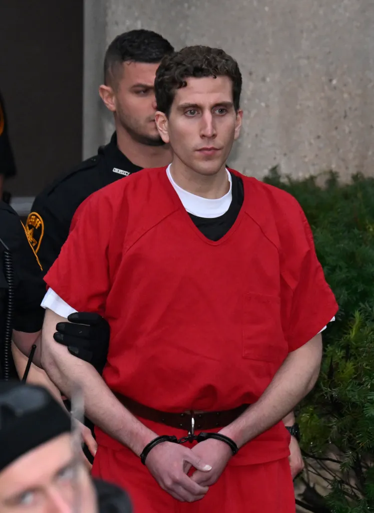 Bryan Kohberger in handcuffs, wearing a red jumpsuit, escorted by a law enforcement officer.