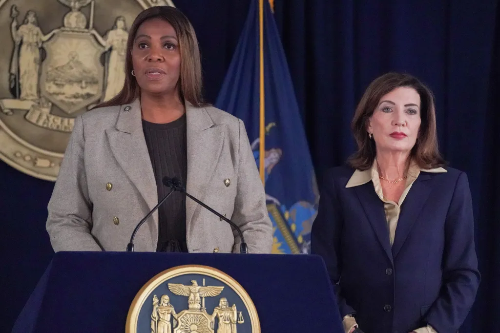 New York Attorney General Letitia James speaks at a podium with New York Governor Kathy Hochul standing beside her.