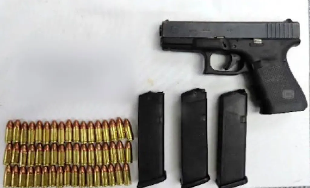A semi-automatic handgun, three magazines, and numerous rounds of ammunition displayed on a flat surface.