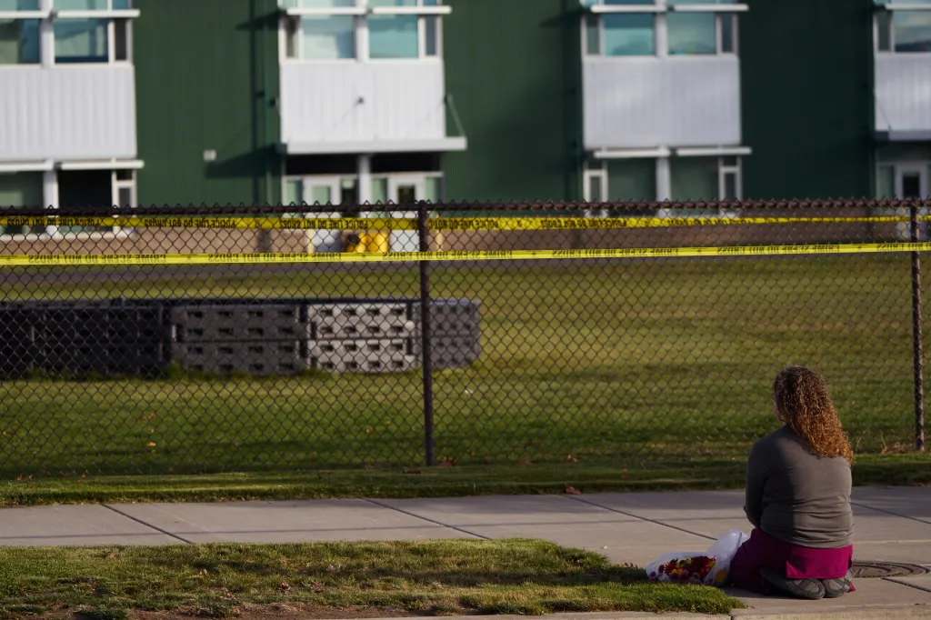 A woman sits on the pavement outside Silver Rail Elementary School with flowers, paying her respects behind police tape.