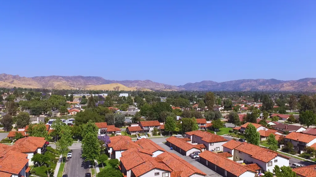 Aerial view of Simi Valley, California, showing residential neighborhoods with red-tiled roofs and distant mountains under a clear blue sky.