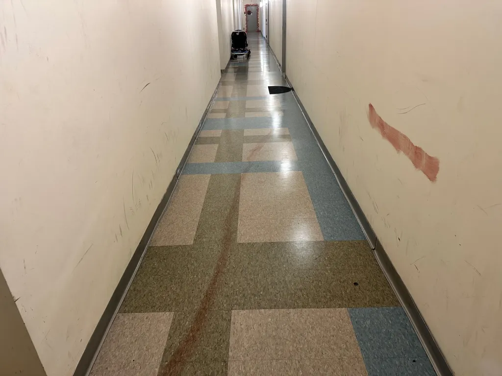 Red stains appear on the floor and wall of a building hallway where a shooting took place.