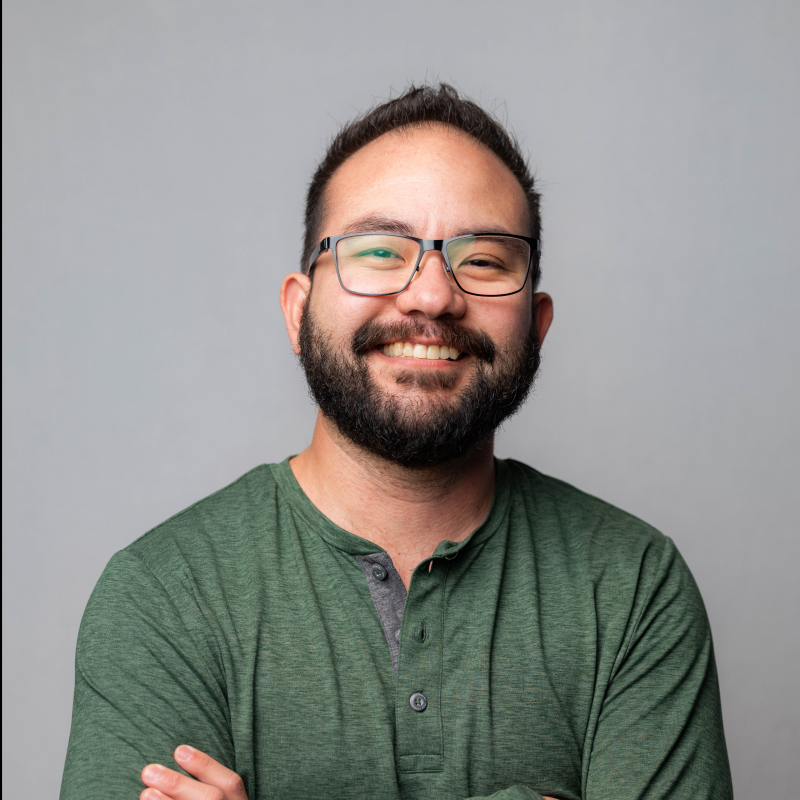 A man with a beard and glasses smiling in a green shirt.