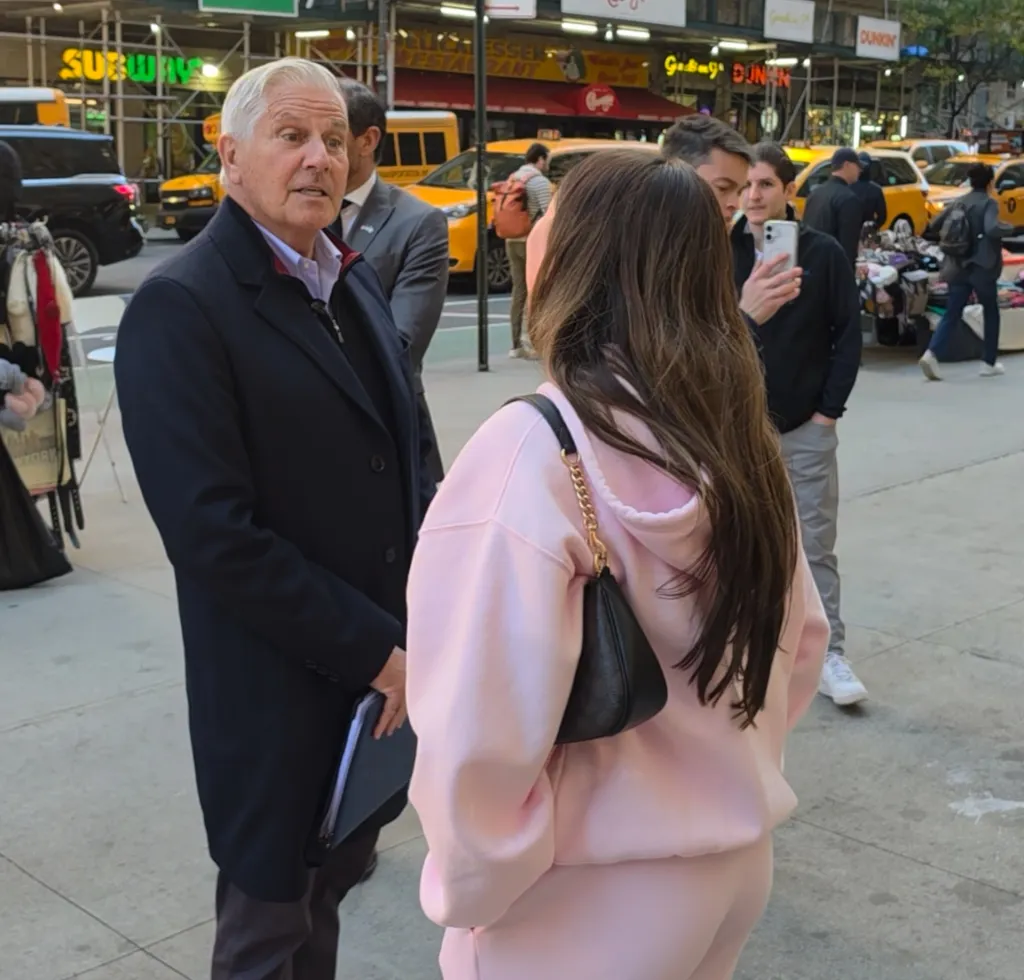 Bruce Blakeman talking to a woman in a pink sweatshirt on a city sidewalk.