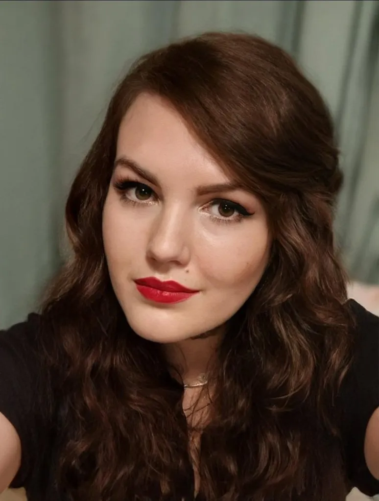 Portrait of Sonia Exelby with brown hair, dark eyeliner, and red lipstick.