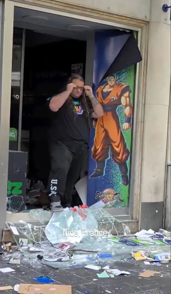 Pierre, a sales assistant, stands in the shattered doorway of his video game store in Nice, France, next to a peeled poster of Goku.