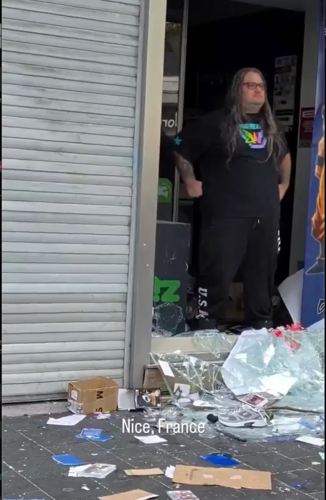 Pierre, a sales assistant, stands in the shattered doorway of a video game store in Nice, France, after rioters attempted to loot the shop.